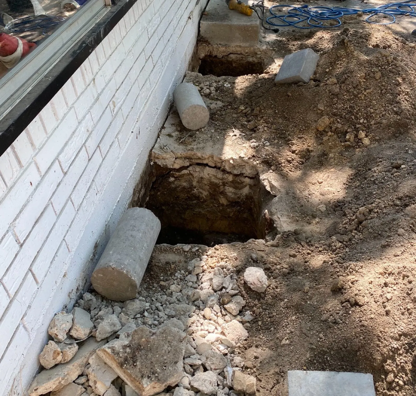 Foundation repair excavation pits with concrete piers staged beside a house